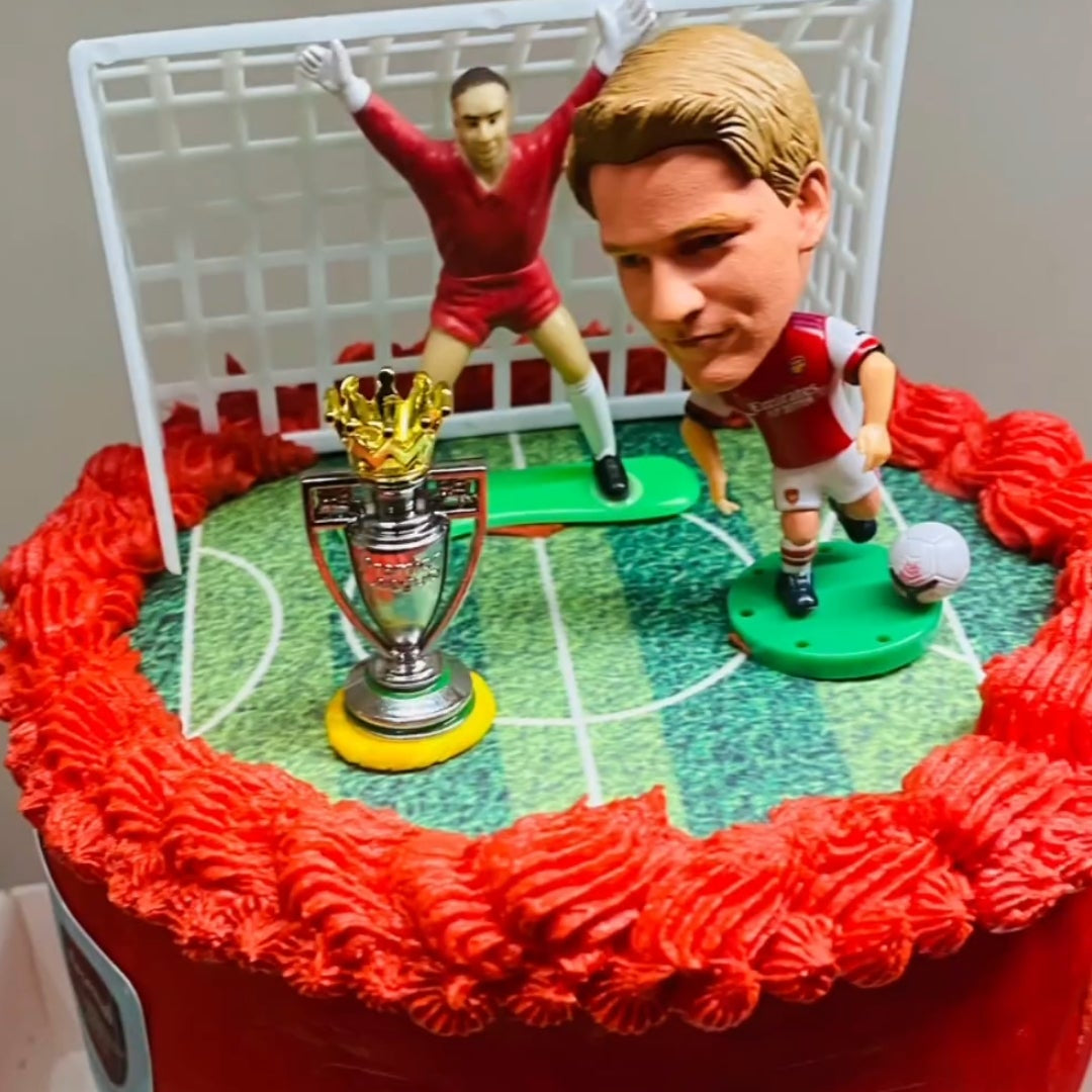 Cake with Arsenal football club branding featuring two figures and a trophy.
